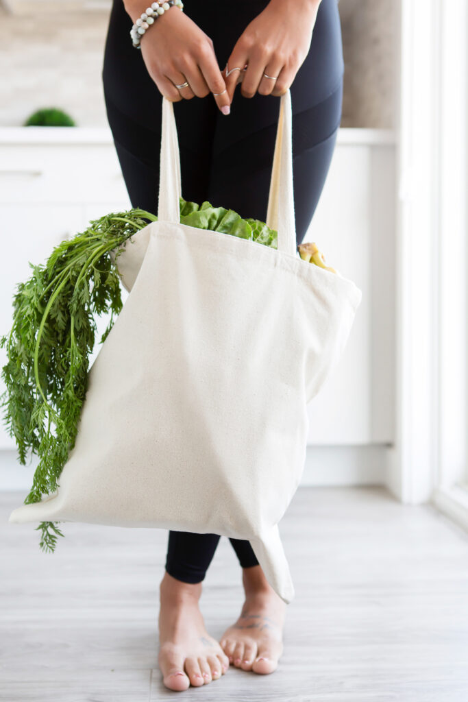 woman standing in the kitchen with her cloth bag full of vegetables that she just bought from the farmers market